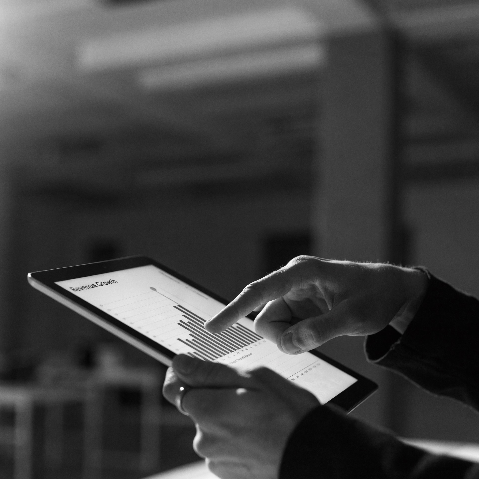 Close-up of a hand pointing at a rising revenue growth bar chart on a tablet screen